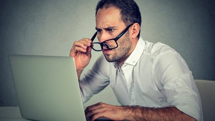 Mann vor Laptop zieht sich Brille ab