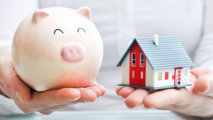 Ein Sparschwein neben einem Modellhaus