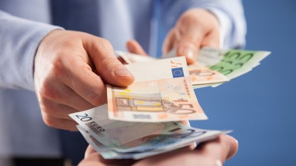 Mann überreicht anderem Mann Geldscheine