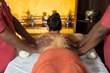 Frau wird von zwei Personen gleichzeitig massiert