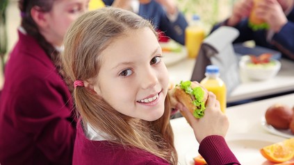 ein Kind in einer Kantine mit einem gesunden Brötchen in der Hand