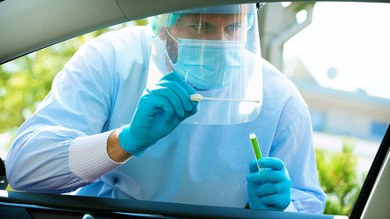 Medizinmitarbeiter lehnt sich mit Corona-Test in ein Auto