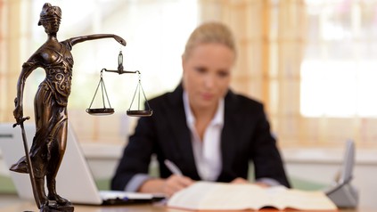 Anwältin sitzt am Schreibtisch, Statue Justita im Vordergrund