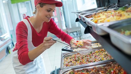 Eine Mensamitarbeiterin füllt ein Gemüsegericht in ein Schälchen