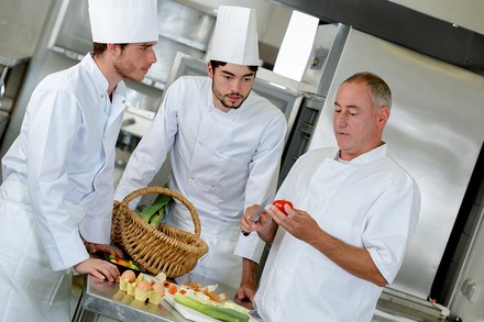 Ein Koch unterrichtet zwei Lehrlinge in Lebensmittelkunde