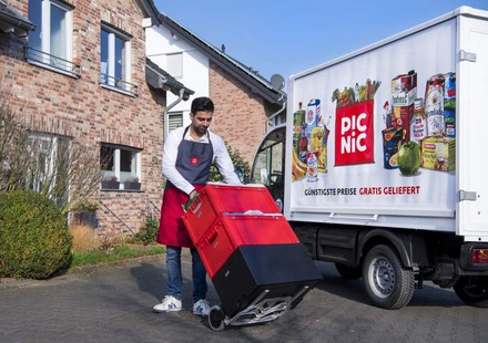Ein Mitarbeiter von Picnic steht mit einigen Waren vor seinem Lieferwagen