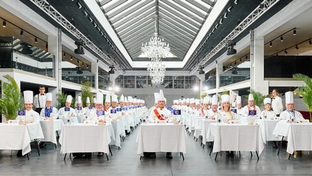 Eine Versammlung von Chefköchen in Kochmontur, sitzend an gedeckten Tischen, bereit, als Jury beim International Taste Institute zu bewerten.