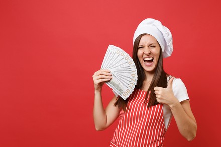 Frau mit Kochmütze hält Geldscheine in der Hand