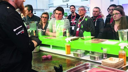 Interessierte Besucher an einem Messestand, bei welchem Fleisch gebraten wird