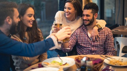 Freundesrunde an einem Esstisch, die mit Bier anstoßen