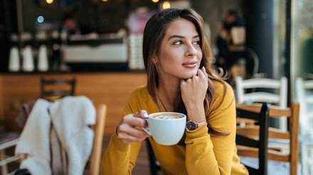 Frau trinkt Kaffee in Café und schaut verträumt aus dem Fenster