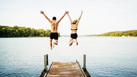 Mann und Frau springen von einem Steg in den See