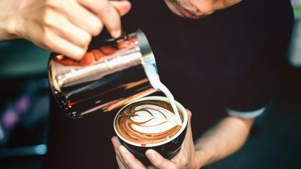 Mann schüttet Milchschaum auf Kaffee