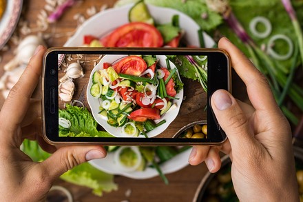 Eine Frau macht ein Handyfoto von einem veganen Essen