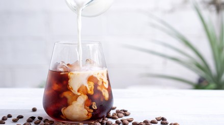 Ein Glas mit Cold Brew in das gerade Milch gegeben wird