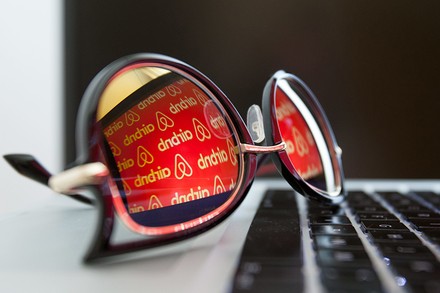 Eine Brille auf einer PC-Tatstatur, in deren Gläsern sich der Schriftzug von „Airbnb“ spiegelt