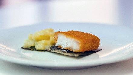 Algenblatt auf dem ein Stück panierter Fisch und Kartoffelsalat liegen