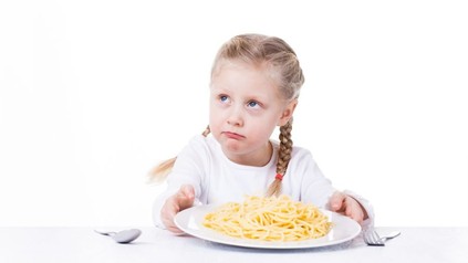 Mädchen mit Teller voller Spaghetti blickt traurig nach oben