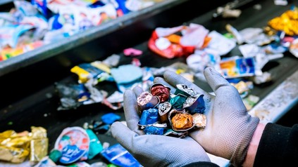 Mann mit Handschuhen hält zerquetschte Kaffeekapseln in der Hand