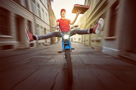 Ein Pizzafahrer auf dem Moped rast durch eine Straße