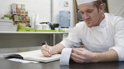 Koch sitzt mit Quittung an Tisch und notiert sich etwas
