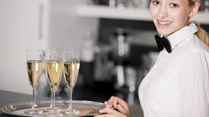 Eine lächelnde Servicekraft mit einem Tablett Sektgläser in der Hand