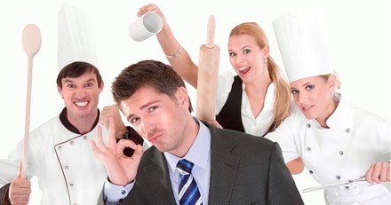 Mann in Anzug signalisiert OK, im Hintergrund Küchenpersonal