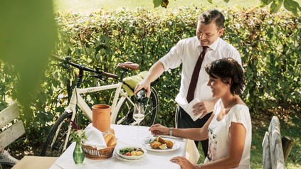 Frau sitzt im Weingarten bei Backhendl und Wein
