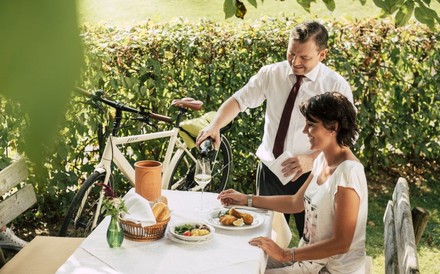 Frau sitzt im Weingarten bei Backhendl und Wein