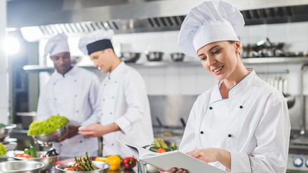 Zwei Köche im Hintergrund und eine Köchin im Vordergrund in der Küche