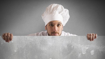 Ein Koch, der vorsichtig hinter einer Mauer hervorschaut