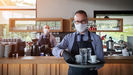 Gastronom mit Maske und Handschuhe hält Tablett