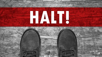 Schuhe von oben, die an einer roten Linie mit dem Wort "Halt!" stehen