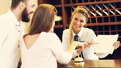 Frau an Rezeption zeigt Gästen etwas auf Zettel