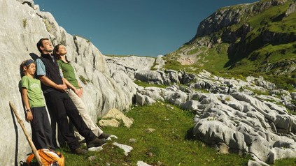 Familie ruht sich beim Wandern an eine Felswand gelehnt aus