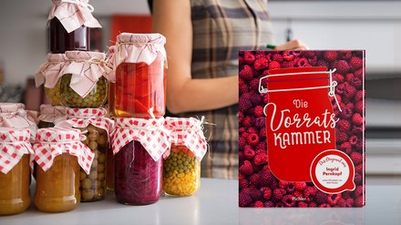 Das Buch „Die Vorratskammer“ steht auf einem Tisch, daneben stehen gefüllte EInmachgläser, im Hintergrund sieht man eine Frau mit Schürze