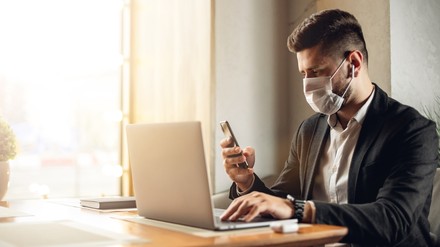 Ein Mann mit Corona Mundschutz an einem Laptop