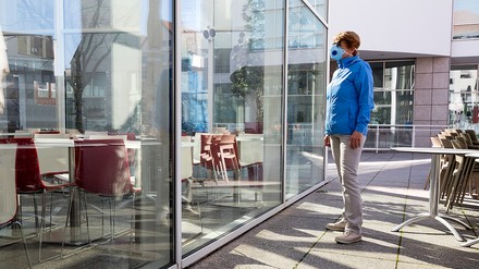 Frau mit Maske steht vor einem geschlossenen Restaurant
