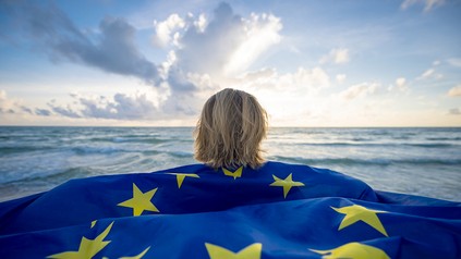 Eine Frau mit EU-Flagge schaut aufs Meer