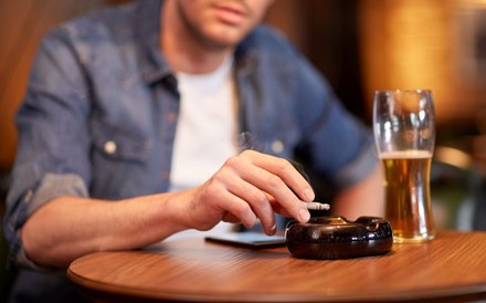Ein Mann sitzt beim Biertrinken an einem Tisch und raucht eine Zigarette