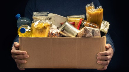 Ein Mann hält eine Box mit Lebensmitteln in den Händen vor einem schwarzen Hintergrund