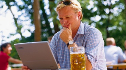 Mann sitzt mit Bier an Laptop