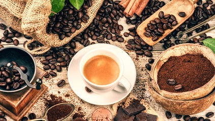 Eine Tasse Kaffee inmitten vieler Kaffeebohnen auf dem Tisch