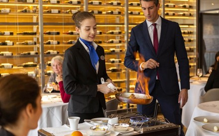 Hotelfachschülerin flambiert im Restaurant eine Speise unter Aufsicht.