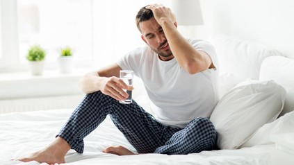 Verkaterter Mann im Bett mit einem Glas Wasser