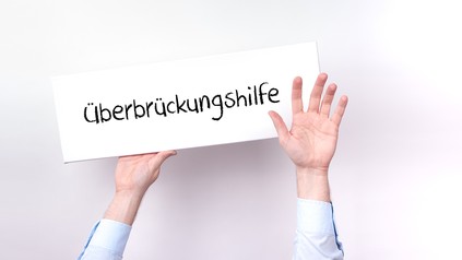 Hände halten Schild mit der Aufschrift "Überbrückungshilfe"