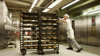 Küchenhilfe schiebt Wagen mit Gebäck