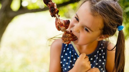 Kind beißt in Fleisch am Spieß