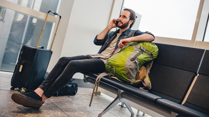 Reisender mit Rucksack und Koffer telefoniert am Flughafen
