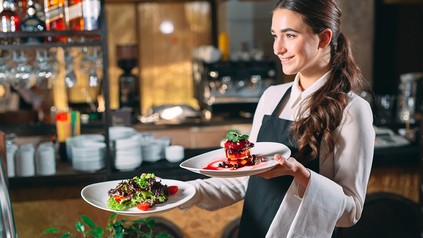 Eine lächelnde Kellnerin trägt Essen durchs Restaurant